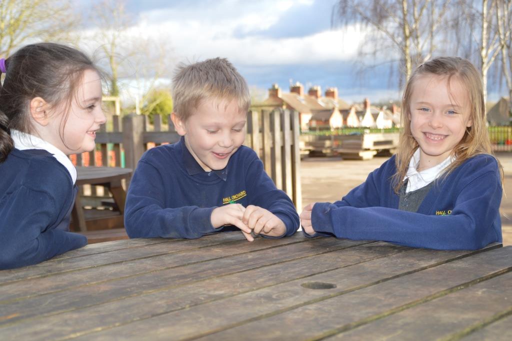 Outside area -3 children sitting and chatting at a round bench in the outside playground